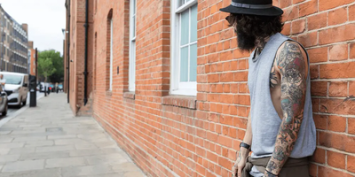 Man with arm tattoos leaning against brick wall