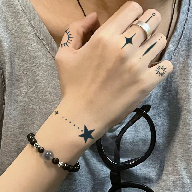 Hand showcasing stylish finger tattoos with geometric shapes and stars, highlighting unique personality and fashion-forward design.